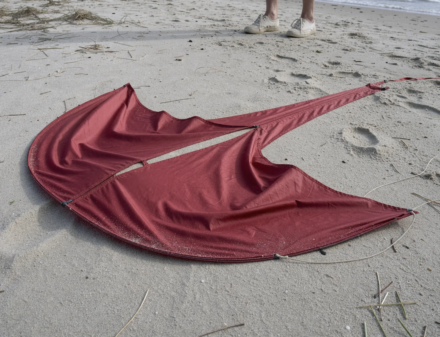 Red silk kite fabric lifted slightly by wind, with open sand between its folds